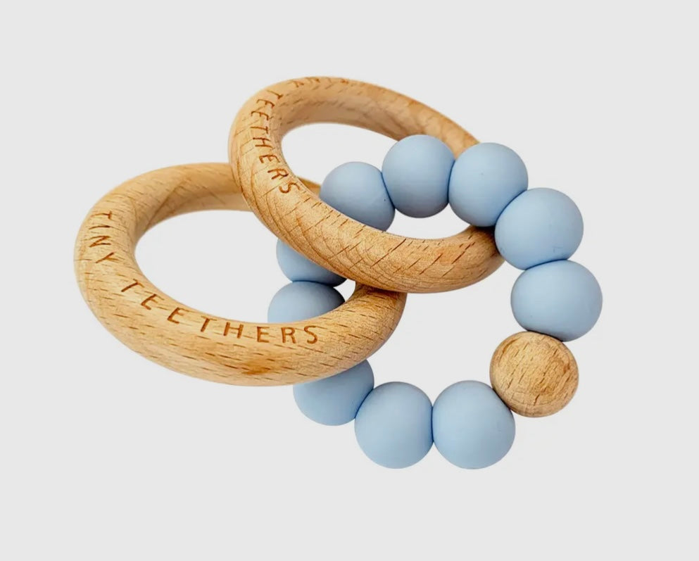 Soothe your baby with Tiny Teethers' pale blue coloured and wood rattle teething rings. Made from 100% silicone and beech wood. Helps baby develop fine motor skills and strength by encouraging grasping, holding and pulling. Also helps with sensory needs by providing them with different textures to keep them stimulated. Perfect for babies aged 3+months.